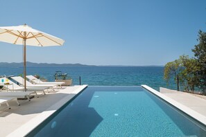 Ein Pool mit Blick auf das Meer und die Berge, Liegestühle und Sonnenschirm.