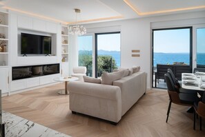 Ein modernes Wohnzimmer mit Sofa, Fernseher und Essbereich, große Fenster mit Meerblick.
