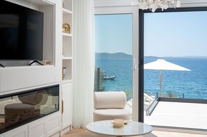 Ein modernes Wohnzimmer mit Fernseher, Sofa und Tisch, mit Blick auf eine Meereslandschaft und Schiffe.