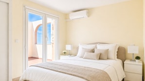 Quarto com cama, duas mesinhas de cabeceira, um criado-mudo, janela com vista e ar condicionado.