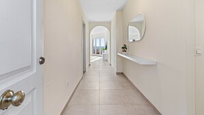 Um corredor com uma porta branca, um espelho e uma planta numa estante.