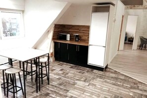 Eine kleine Küche mit einem weißen Kühlschrank, schwarzen Schränken, einer Holz Arbeitsplatte und einem Essbereich mit Hockstühlen.