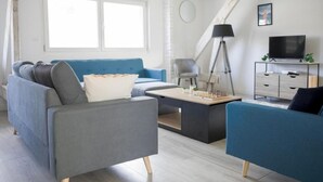 Moderni olohuone, jossa on sininen sohva, harmaa nojatuoli, sohvapöytä, televisio ja lamppu.