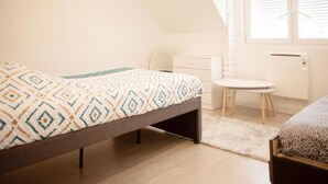 Makuuhuoneessa on sänky, pieni työpöytä, tuoli ja ikkuna, jossa on sälekaihtimet.