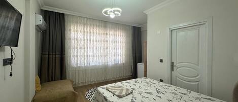 Ein Schlafzimmer mit Bett, einem an der Wand montierten Fernseher, einer Klimaanlage, einer Tür und einem Fenster mit Vorhängen.