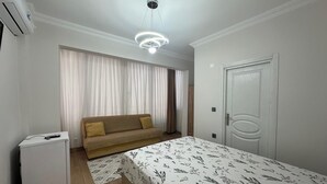 A bedroom with a bed, a sofa, a small white cabinet, and a door. - MÜREFTE SUİTE (Sarkoy)