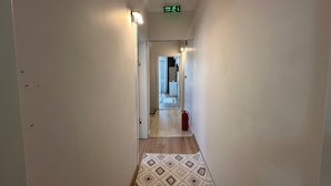 A hallway with a patterned rug, a red trash bin, and an exit sign. - MÜREFTE SUİTE (Sarkoy)