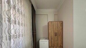 A small room with a wooden wardrobe, a white refrigerator, and a patterned curtain. - MÜREFTE SUİTE (Sarkoy)