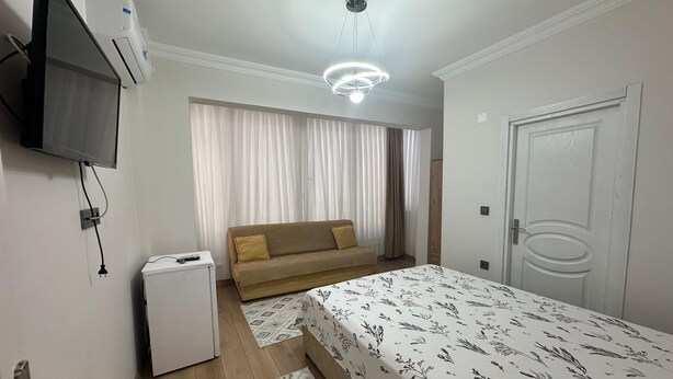 A bedroom with a bed, a sofa, a TV, an air conditioning unit, and a door. - MÜREFTE SUİTE (Sarkoy)
