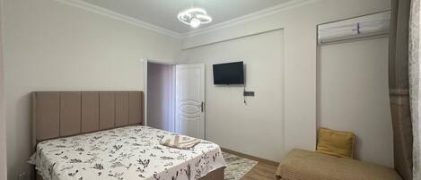 A bedroom with a bed, bedside table, TV, wardrobe, and a small seating area.