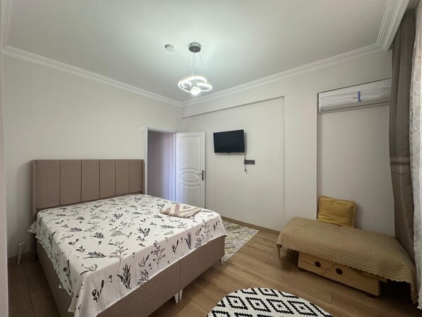 Un dormitorio con cama, mesita de noche, televisor, armario y una pequeña zona de estar.