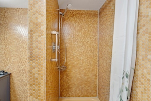 Une douche équipée d’un pommeau de douche à main, d’un espace de douche clos par des parois de verre et d’un mur carrelé orné d’un motif en nid d’abeille.