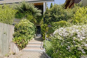 Un escalier en pierre menant à une porte en bois, entouré d’une végétation luxuriante et de fleurs blanches.
