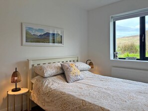 Une chambre à coucher avec un lit, un tableau au mur, une fenêtre donnant sur la plage et une lampe sur une table de chevet.