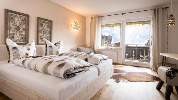 A bedroom with a large bed, a view of the city, and a balcony.