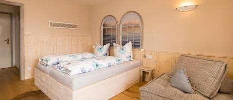 A bedroom with a bed, a sofa, a small table, and two arched windows.