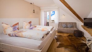 A bedroom with a bed, a sofa, a television, and a window with curtains.
