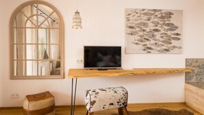 A room with a large arched window, a wooden desk with a television, a cowhide chair, and a fish-themed artwork on the wall.