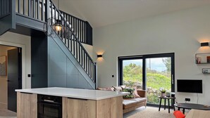 Une cuisine moderne dotée d’un îlot central, d’un escalier, d’un coin salon avec vue et d’un espace repas avec des chaises rouges.