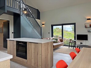 A modern kitchen with a central island, a staircase, a seating area with a view, and a dining space with red chairs. - Cottage 505 - Roundstone - sleeps 8 guests  in 4 bedrooms (Roundstone)