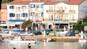 Une propriété située au bord de l’eau, dotée de plusieurs balcons, d’un port de plaisance avec des bateaux et d’une enseigne indiquant « Appartements Toni ».