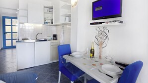 Une cuisine moderne avec des meubles blancs, une table à manger pour deux personnes et un téléviseur à écran plat fixé au-dessus du comptoir.