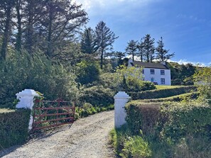 A white building with a red roof, surrounded by greenery and a gravel path leading to a gated entrance. - Cottage 507 - Renvyle - sleeps 6 guests  in 3 bedrooms (Renvyle)
