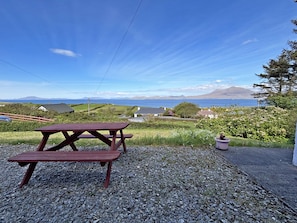 A picnic table on a gravel area with a view of a coastal landscape, including houses and a mountain in the distance. - Cottage 507 - Renvyle - sleeps 6 guests  in 3 bedrooms (Renvyle)