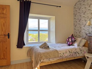 A bedroom with a bed, a window with a view, a wooden door, and a lamp. - Cottage 507 - Renvyle - sleeps 6 guests  in 3 bedrooms (Renvyle)