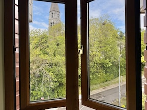 Ein Fenster mit Blick auf ein Gebäude mit einem Glockenturm, umgeben von Bäumen und einer Straße.