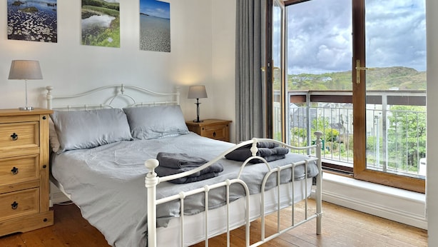 A bedroom with a bed, two bedside tables, a window with a view, and three wall-mounted pictures. - Apartment 514 - Clifden - sleeps 6 guests  in 3 bedrooms (Clifden)