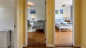 A hallway leading to two bedrooms with wooden flooring, white beds, and bedside lamps. - Apartment 514 - Clifden - sleeps 6 guests  in 3 bedrooms (Clifden)