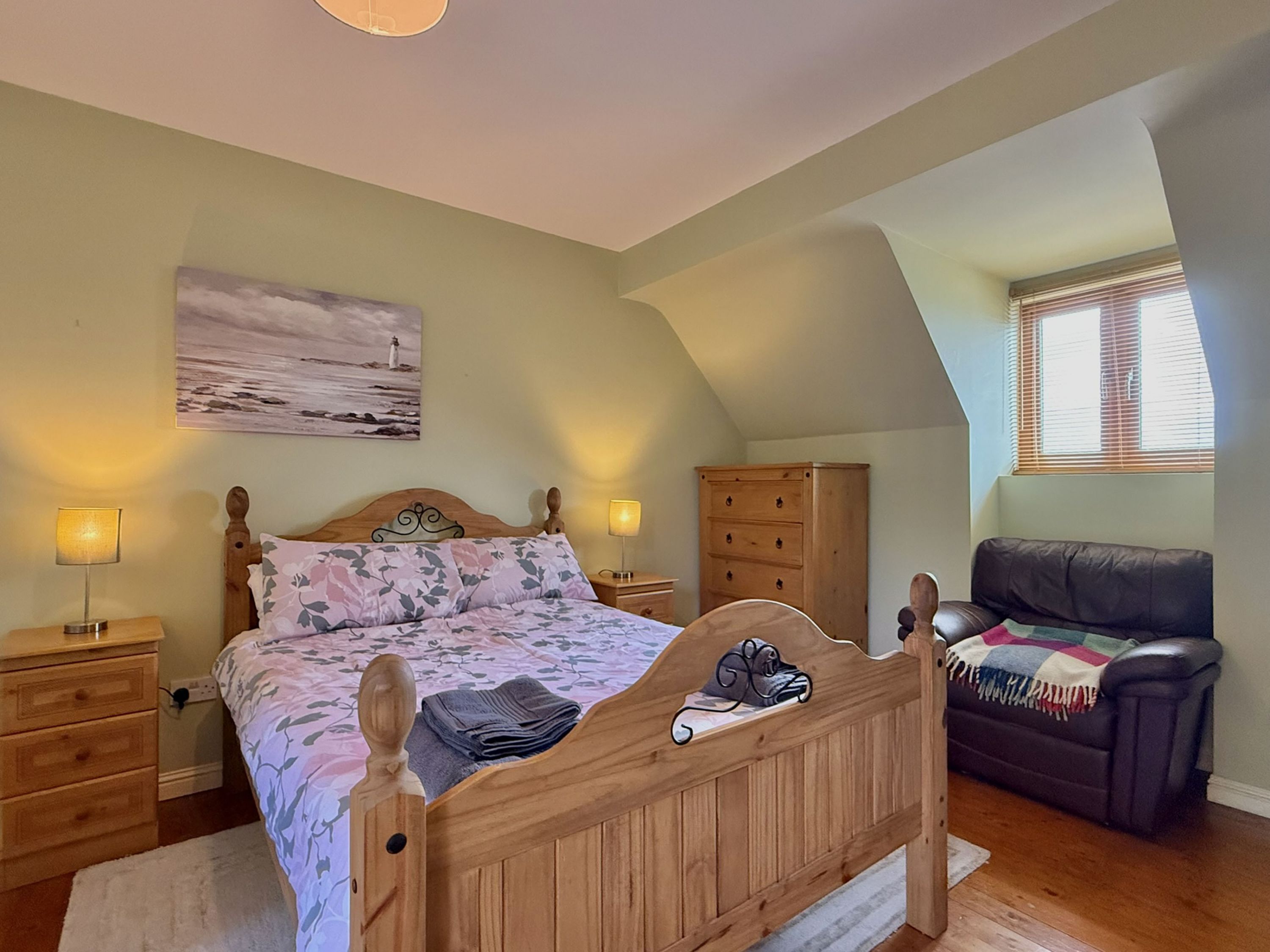 A bedroom with a wooden bed, bedside lamps, a dresser, a sofa, and a painting on the wall.