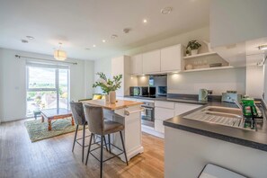 A modern kitchen with a central island, built-in appliances, and a view to the outside. - Bright & Modern 1BDR Flat in New Malden (New Malden)