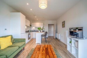 A modern apartment with a green sofa, a wooden rug, a kitchen with white cabinets, and a TV on a white stand. - Bright & Modern 1BDR Flat in New Malden (New Malden)