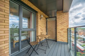 A balcony with a wooden table and chairs, large windows, and a brick wall. - Bright & Modern 1BDR Flat in New Malden (New Malden)