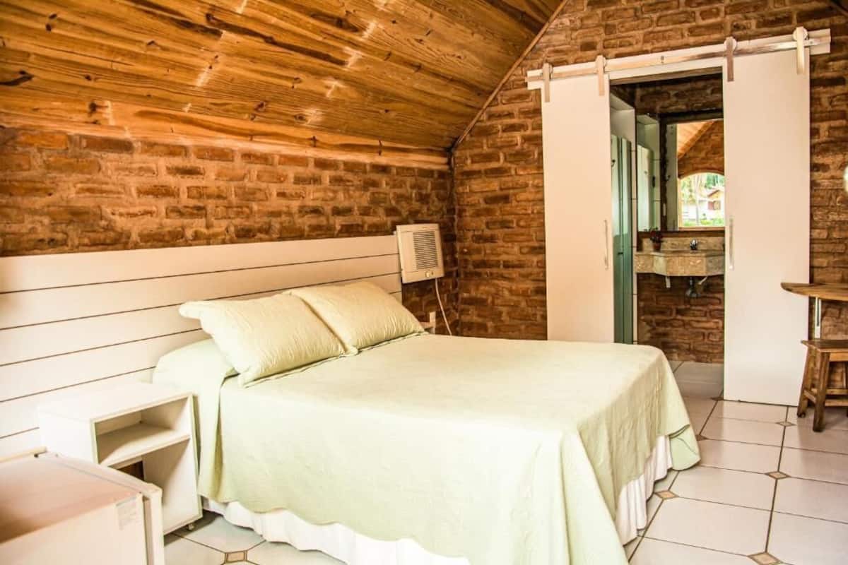 Una habitación con una cama, techo de madera, pared de ladrillo, puerta blanca y una pequeña mesa.