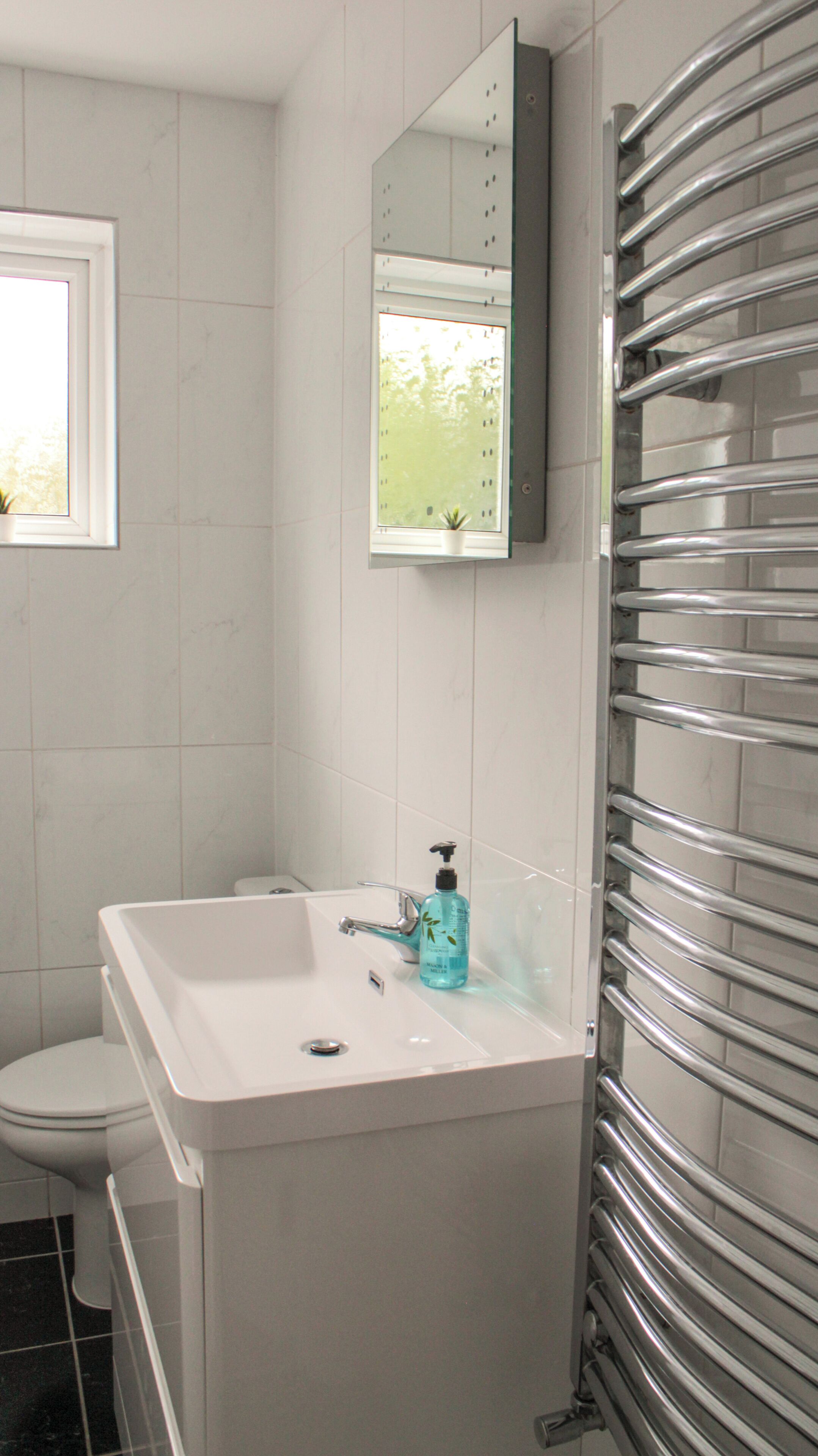 Une salle de bain avec un lavabo blanc, un miroir, une fenêtre et un porte-serviettes.