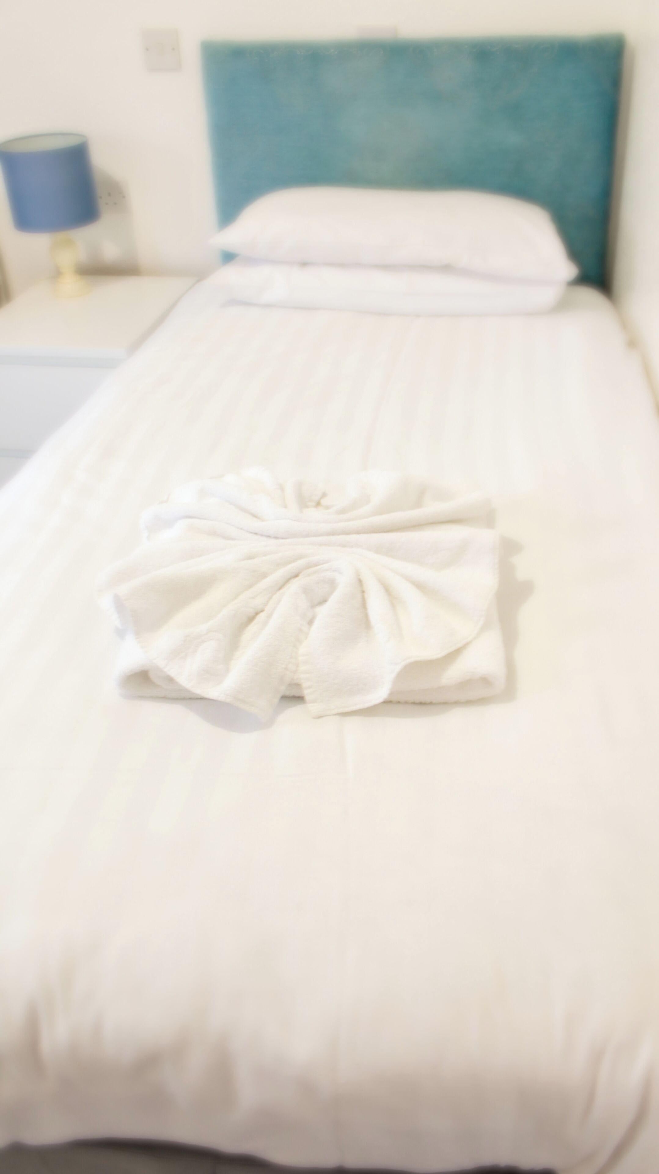 A neatly made bed with a white duvet and a towel arranged in a bow.