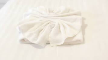 A neatly made bed with a white duvet and a towel arranged in a bow.