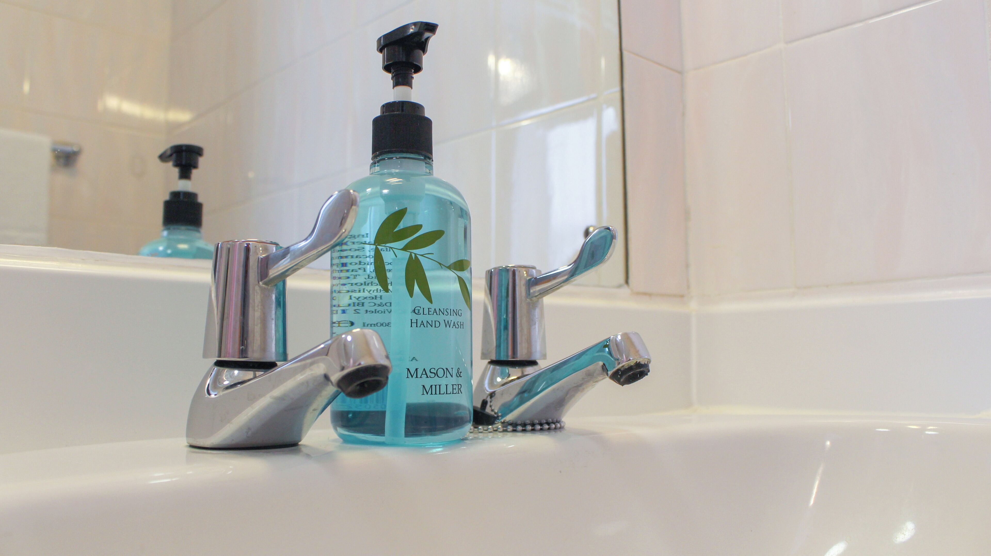 A bathroom with a white sink, a blue hand wash bottle, and a chrome faucet.