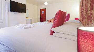 A hotel room with a bed, a flat-screen TV mounted on the wall, a door, and a bedside lamp.