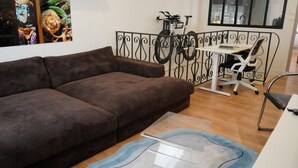 Een bruine bank, een glazen bijzettafeltje, een wit bureau met een stoel, en een fiets op de achtergrond.