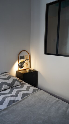 Une chambre à coucher comprenant un lit, une table de chevet, une lampe, un tableau encadré et un tél éviseur fixé au mur.