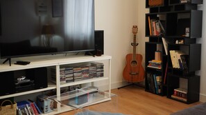 Ein Wohnzimmer mit Fernseher, Bücherregalen, einer Gitarre und einem durchsichtigen Kunststoff-Aufbewahrungsfach.