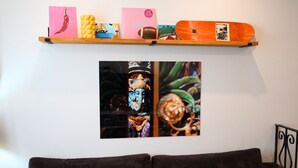 Een wand met een plank waarop verschillende voorwerpen staan, een lijst met een kunstwerk en een zwarte metalen stoel.