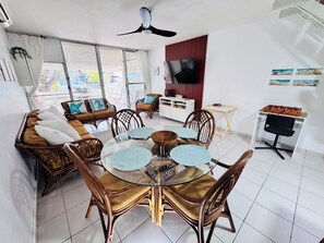 Un salon moderne avec une table à manger en verre, des meubles en osier, un téléviseur et un rideau rouge.