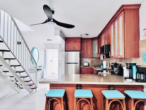 A kitchen with a central island, stainless steel appliances, wooden cabinets, and a ceiling fan.