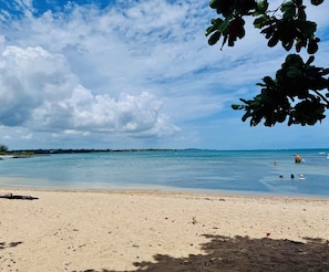 A beach with clear water, a sandy shore, and a distant shoreline.