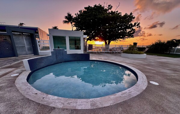 Une piscine au design moderne, entourée d’une terrasse dallée et d’une clôture blanche.